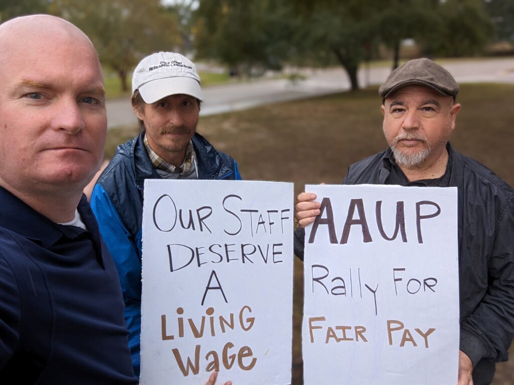 Michael McGill stands alongside two protesters holding signs advocating for fair pay and workers' rights