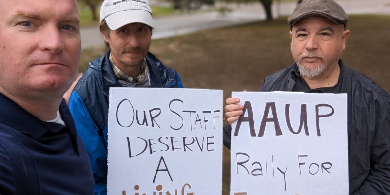 Michael McGill stands alongside two protesters holding signs advocating for fair pay and workers' rights