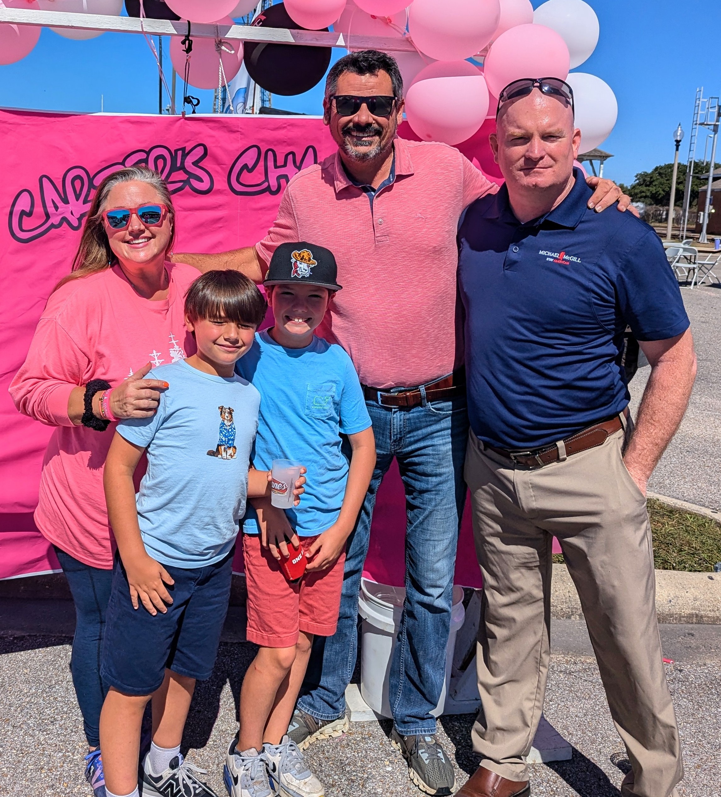 Carrie Duncan, Dan Cuevas, Michael McGill are at the Pink Dress Run in Gulfport, MS they are standing in front of a pink banner that says Carters Champions