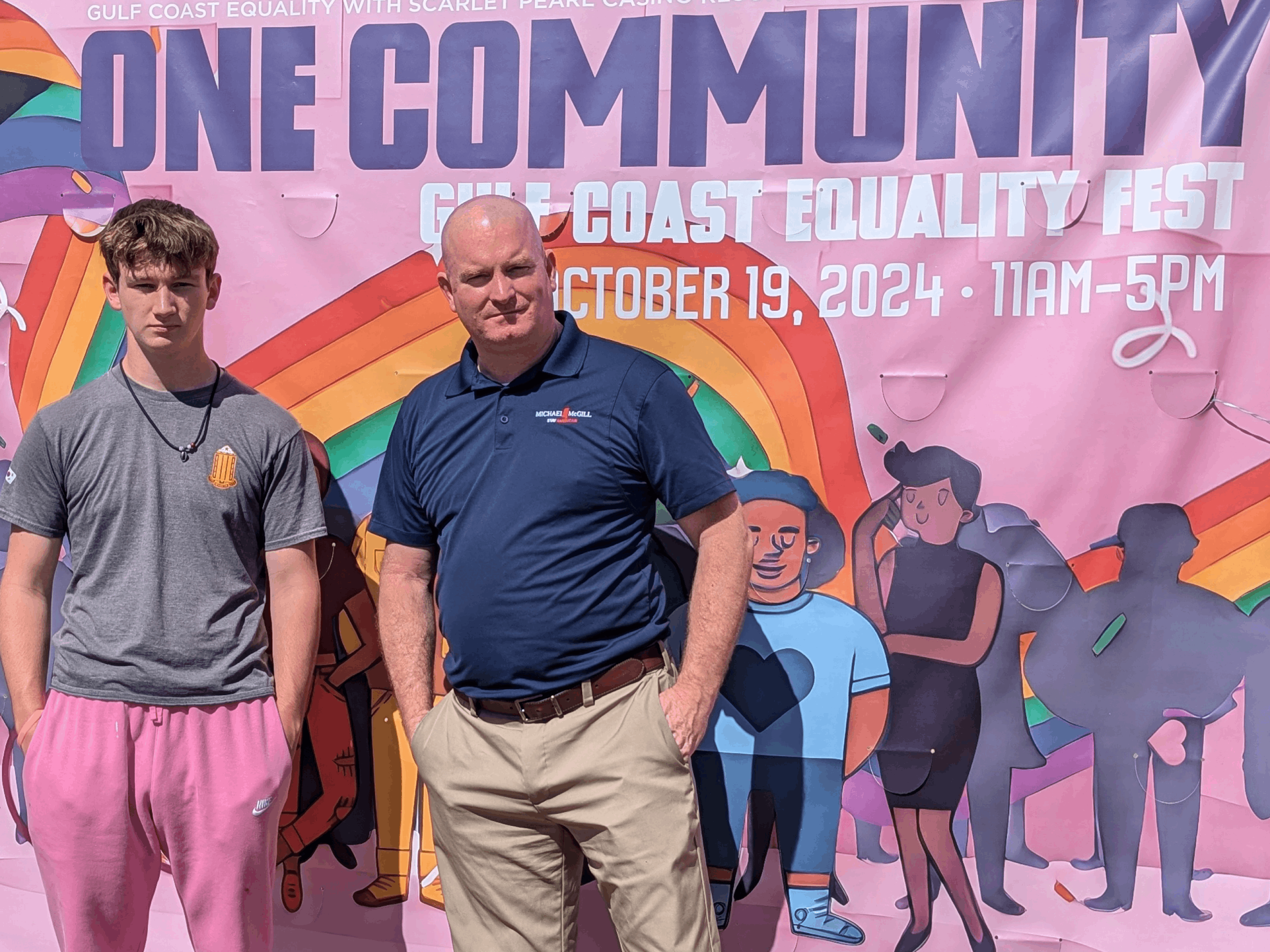 Michael McGill and his son stand infront of the One Community sign at the Gulf Coast Equality Fest 2024 in Biloxi, MS