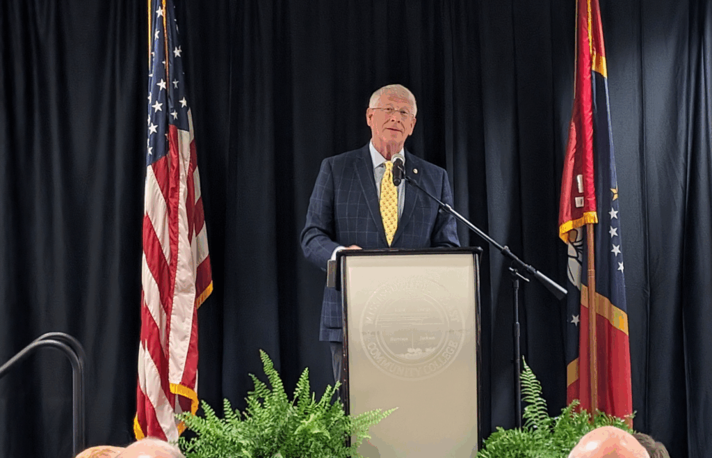 Wicker 2 U.S. Senator Roger Wicker stands at a podium delivering remarks during the 2025 Legislative Luncheon in Biloxi, Mississippi, flanked by American and Mississippi state flags, with attendees seated and listening in the foreground.