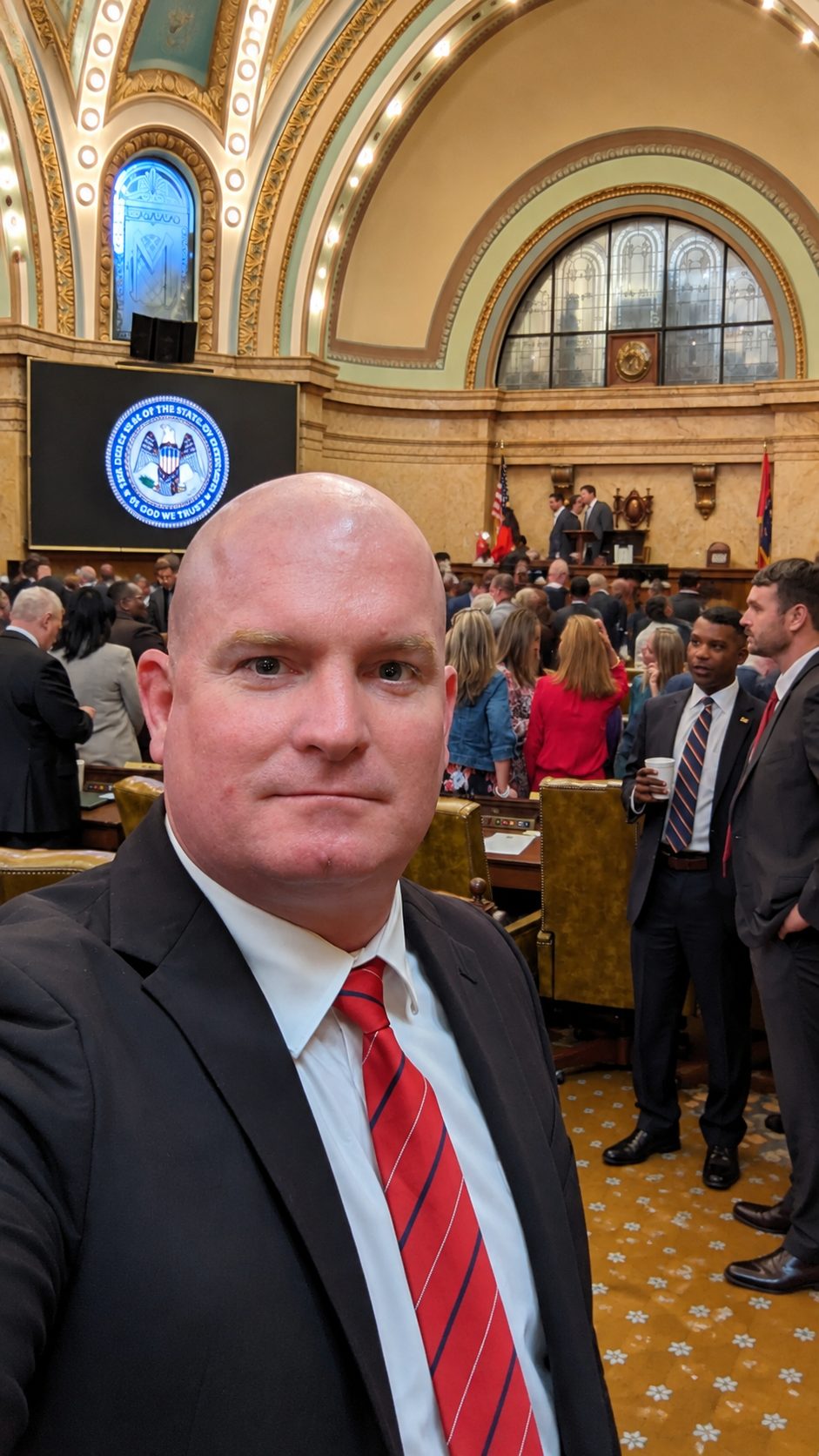 Michael McGill takes a selfie in the Mississippi House chamber with legislators and visitors standing behind him